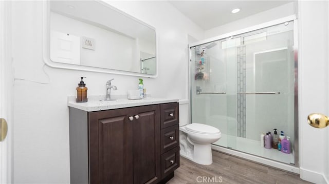 bathroom with toilet, recessed lighting, wood finished floors, vanity, and a shower stall