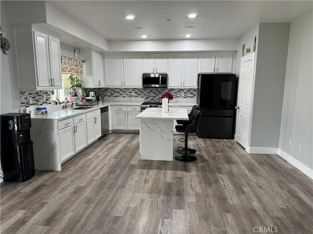 kitchen with wood finished floors, a kitchen island, a sink, white cabinets, and appliances with stainless steel finishes