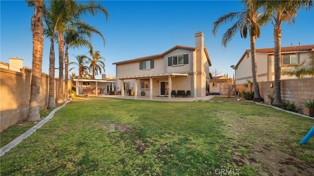 back of house with a patio, a fenced backyard, a lawn, stucco siding, and a chimney