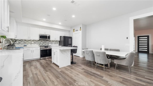 kitchen featuring stainless steel appliances, tasteful backsplash, visible vents, white cabinets, and a sink