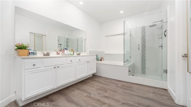 bathroom with a garden tub, a sink, wood finished floors, a shower stall, and double vanity