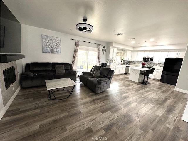 living area with a glass covered fireplace, dark wood finished floors, visible vents, and baseboards