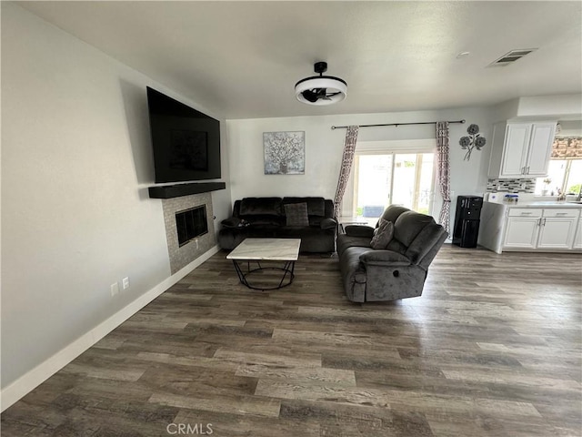 living room with a glass covered fireplace, visible vents, dark wood finished floors, and baseboards