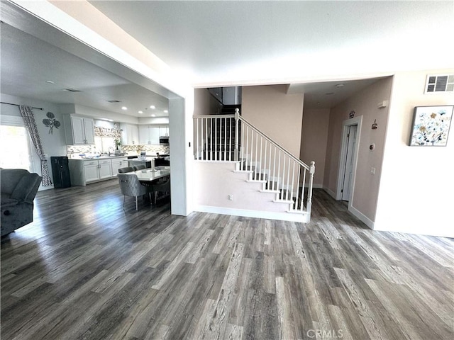 unfurnished living room with dark wood-style flooring, visible vents, stairway, and baseboards