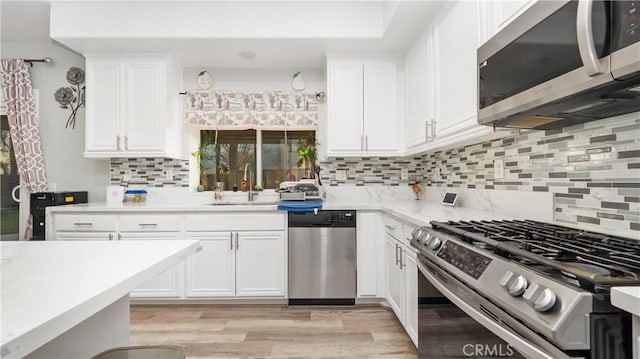 kitchen featuring appliances with stainless steel finishes, white cabinets, a sink, and tasteful backsplash