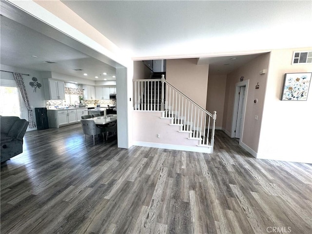 unfurnished living room with dark wood-type flooring, visible vents, stairway, and baseboards