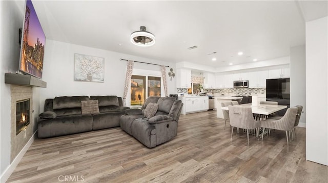 living room featuring baseboards, visible vents, a glass covered fireplace, light wood-style floors, and recessed lighting