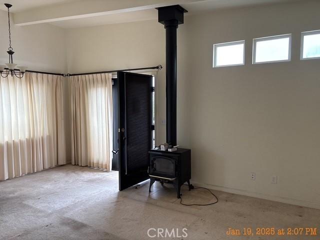 living room featuring beamed ceiling, a wood stove, light carpet, and a notable chandelier