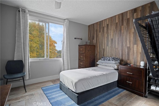 bedroom featuring ceiling fan, light hardwood / wood-style flooring, a textured ceiling, and wood walls