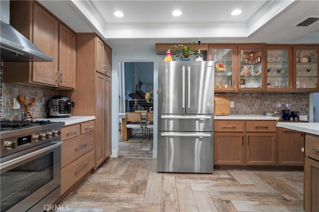 kitchen featuring wall chimney exhaust hood, stainless steel appliances, a tray ceiling, and light parquet floors