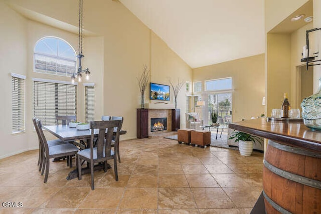 dining area featuring a high ceiling, a tiled fireplace, and an inviting chandelier