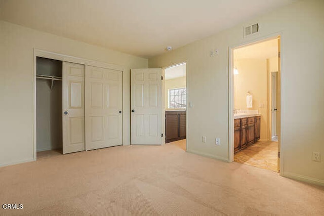 unfurnished bedroom with a closet, visible vents, light carpet, and ensuite bath