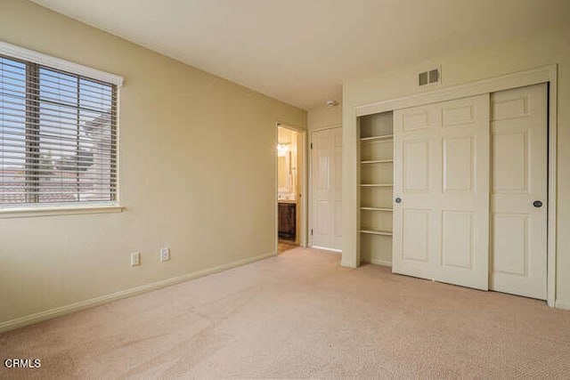 unfurnished bedroom with ensuite bathroom, light carpet, visible vents, baseboards, and a closet