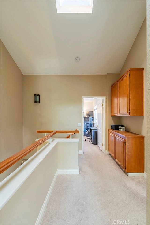 corridor featuring light carpet, vaulted ceiling with skylight, an upstairs landing, and baseboards