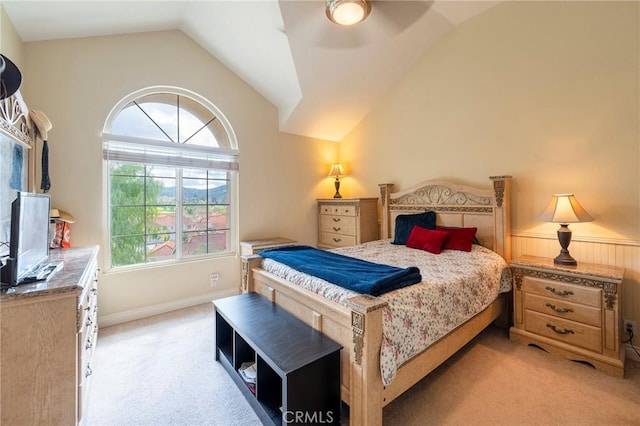 bedroom featuring lofted ceiling, a wainscoted wall, a ceiling fan, and light colored carpet