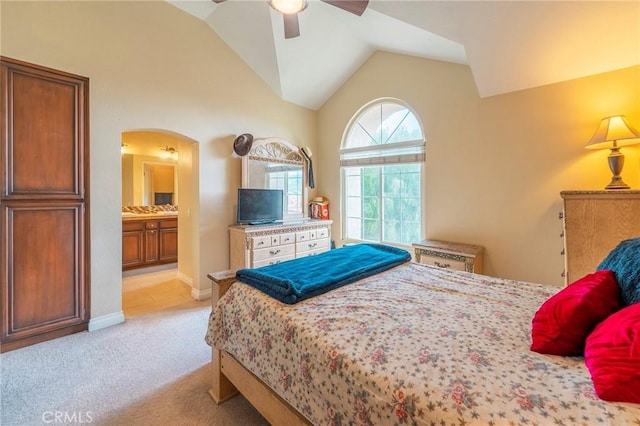 bedroom featuring arched walkways, lofted ceiling, light colored carpet, ensuite bath, and baseboards