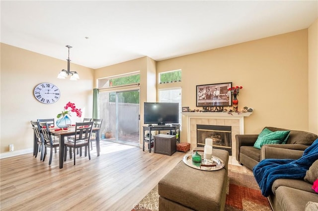 living room featuring a tiled fireplace, a notable chandelier, and light hardwood / wood-style flooring