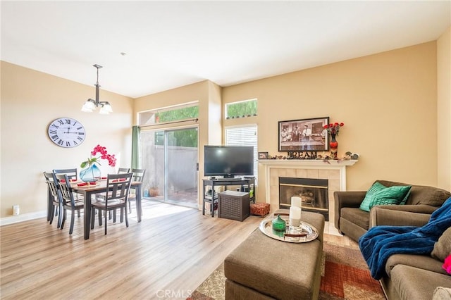 living room with light wood-type flooring, baseboards, a chandelier, and a tile fireplace