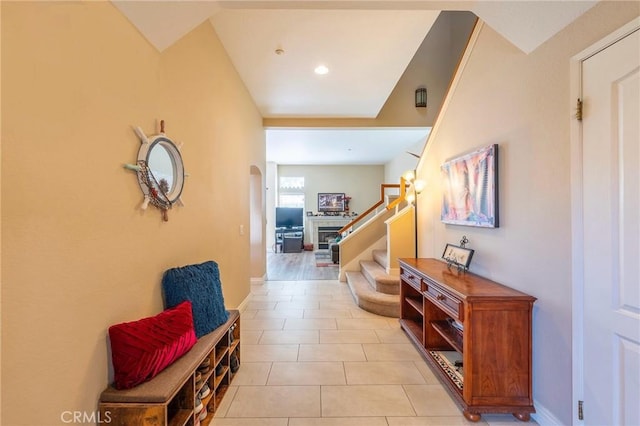 hall featuring light tile patterned floors, baseboards, stairway, and arched walkways