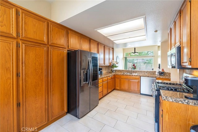 kitchen featuring light tile patterned floors, stainless steel appliances, a sink, backsplash, and brown cabinetry