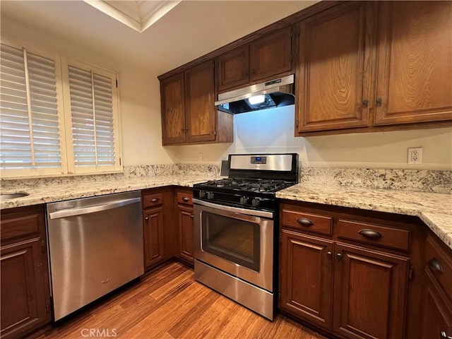 kitchen featuring under cabinet range hood, appliances with stainless steel finishes, light wood-style floors, and light stone countertops