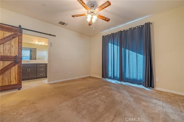 unfurnished room with light colored carpet, a barn door, and ceiling fan