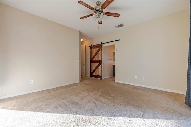 unfurnished room with light colored carpet, a barn door, and ceiling fan