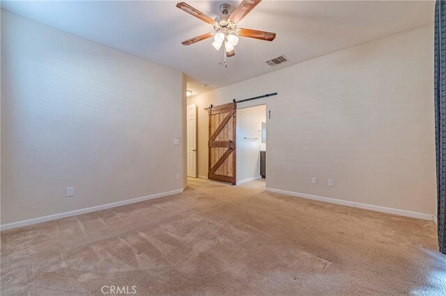 carpeted spare room featuring ceiling fan and a barn door