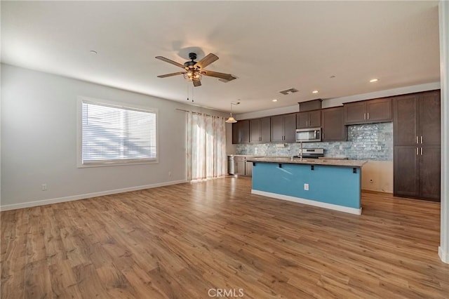 kitchen with tasteful backsplash, appliances with stainless steel finishes, a center island with sink, and light wood-type flooring