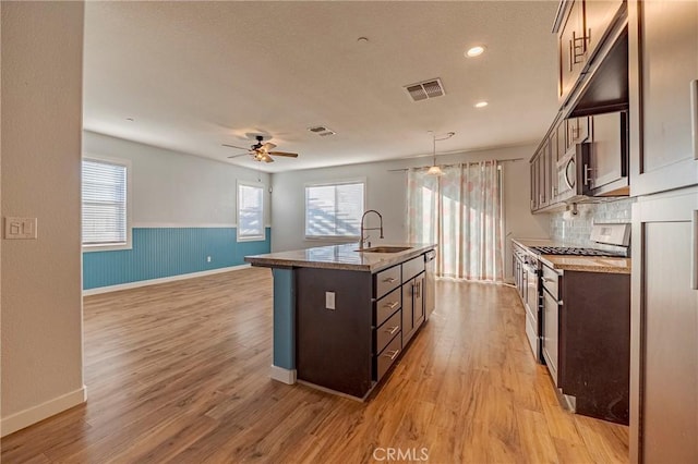 kitchen featuring pendant lighting, sink, light stone counters, dark brown cabinetry, and a center island with sink