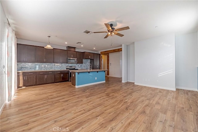 kitchen with appliances with stainless steel finishes, hanging light fixtures, tasteful backsplash, light hardwood / wood-style floors, and a center island with sink