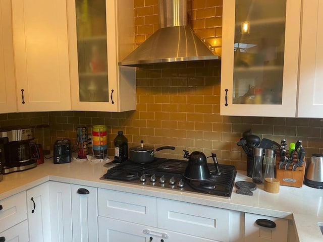 kitchen featuring tasteful backsplash, wall chimney range hood, and white cabinets