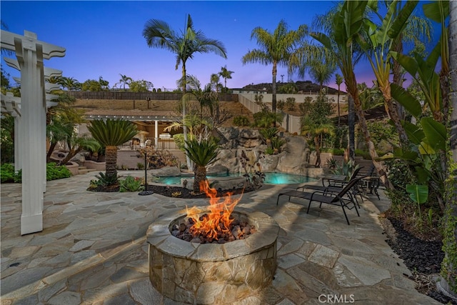 patio terrace at dusk with a fenced in pool and a fire pit