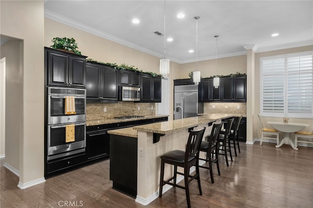 kitchen with decorative light fixtures, a kitchen bar, a kitchen island with sink, stainless steel appliances, and dark wood-type flooring