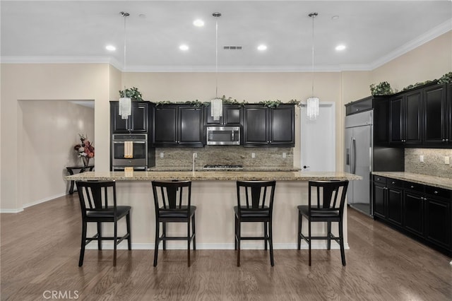 kitchen featuring a kitchen island with sink, decorative light fixtures, stainless steel appliances, and a breakfast bar