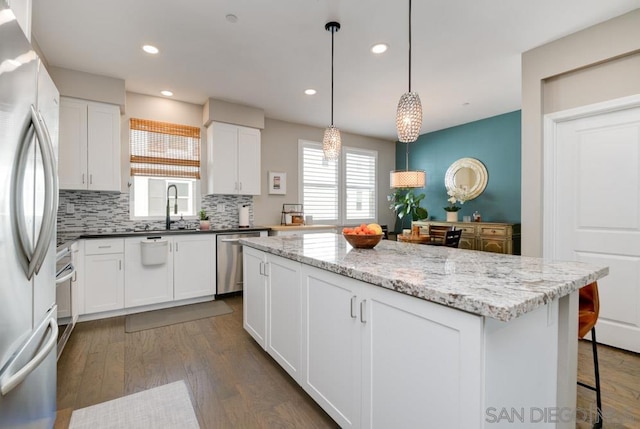 kitchen featuring appliances with stainless steel finishes, white cabinetry, hanging light fixtures, dark hardwood / wood-style flooring, and dark stone counters