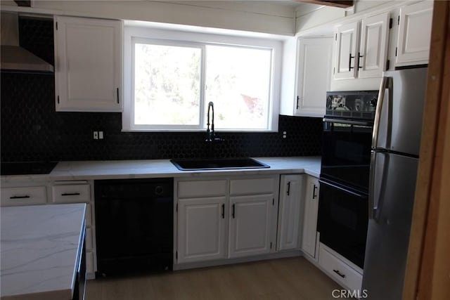 kitchen featuring sink, white cabinetry, tasteful backsplash, black appliances, and wall chimney range hood