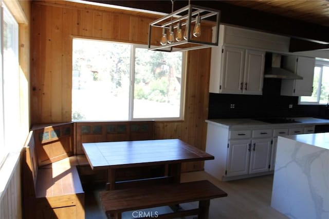 kitchen featuring white cabinetry, hanging light fixtures, breakfast area, a healthy amount of sunlight, and wall chimney exhaust hood