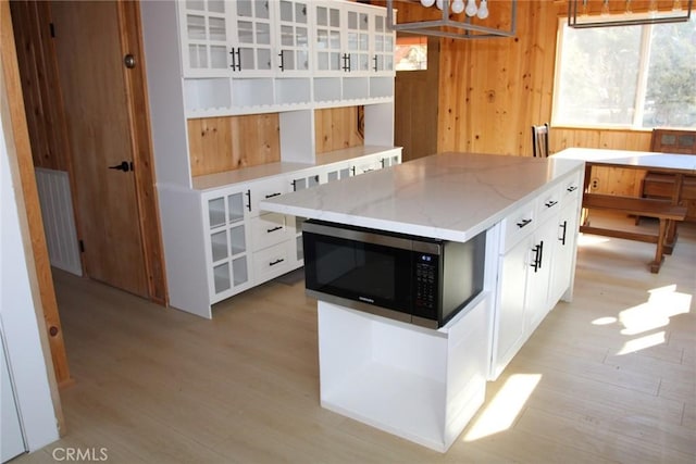 kitchen featuring light stone countertops, a center island, white cabinets, and wood walls