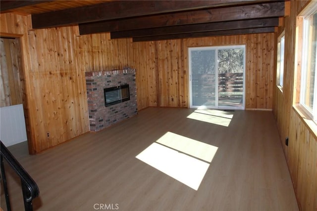 unfurnished living room featuring wood walls, a fireplace, beam ceiling, and light hardwood / wood-style floors