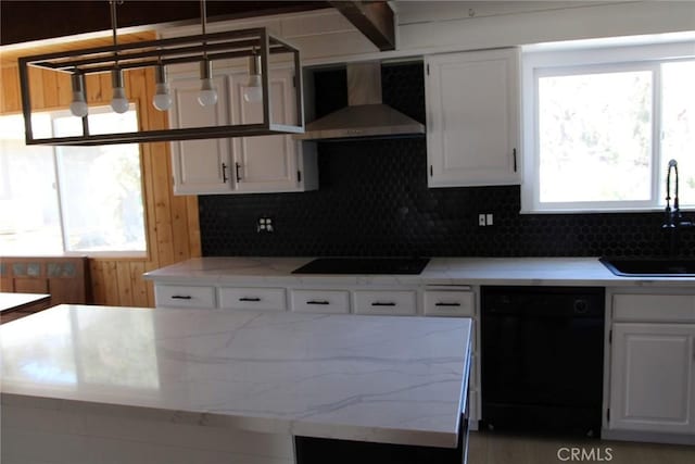 kitchen featuring sink, black appliances, hanging light fixtures, wall chimney range hood, and white cabinets