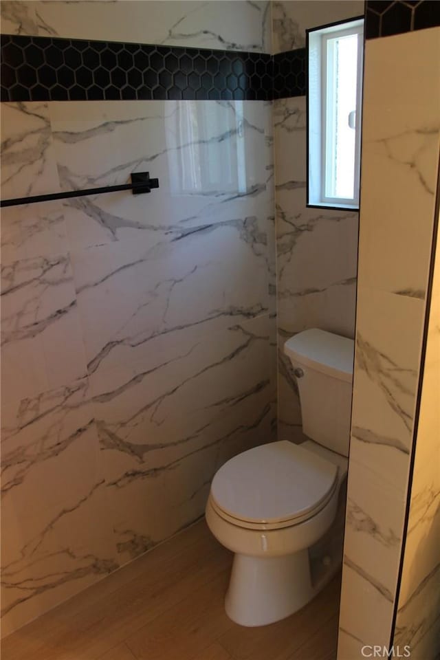 bathroom featuring hardwood / wood-style flooring, toilet, and tile walls