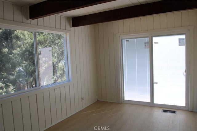 spare room with beam ceiling, wooden walls, and light hardwood / wood-style floors