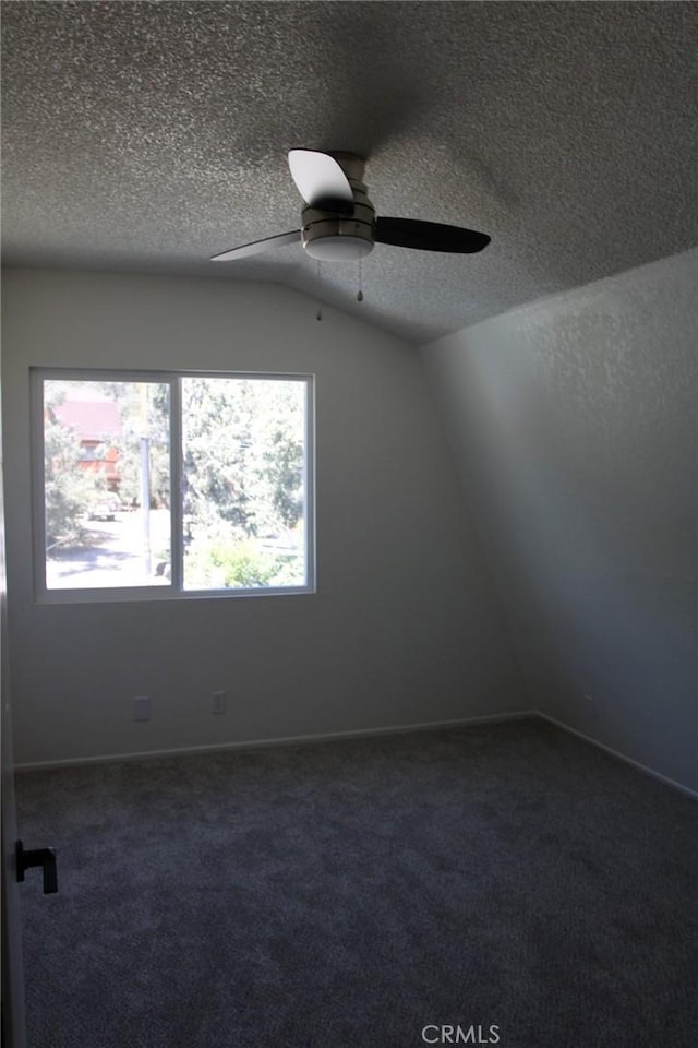 unfurnished room featuring lofted ceiling, dark carpet, and a textured ceiling