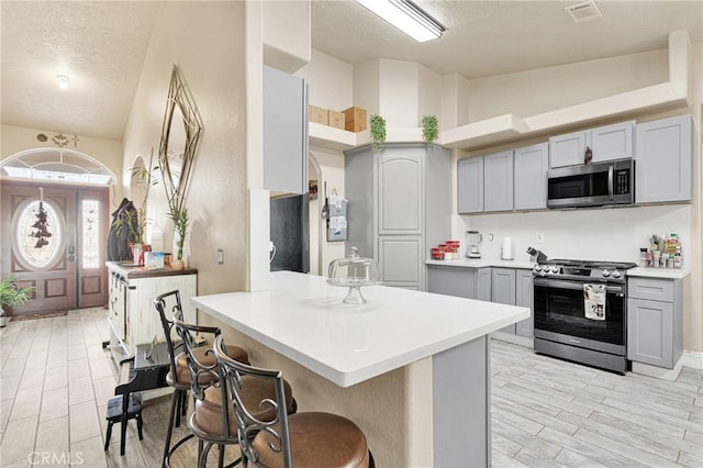 kitchen with vaulted ceiling, a breakfast bar area, gray cabinetry, stainless steel appliances, and a textured ceiling