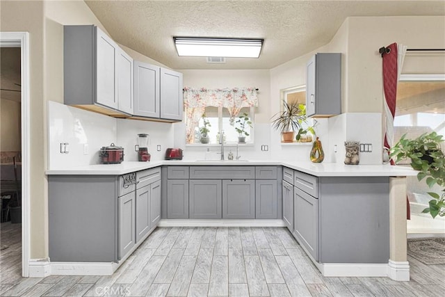 kitchen with sink, a textured ceiling, gray cabinets, kitchen peninsula, and light hardwood / wood-style floors