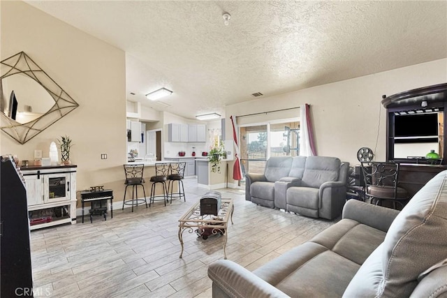 living room with lofted ceiling, a textured ceiling, and light wood-type flooring