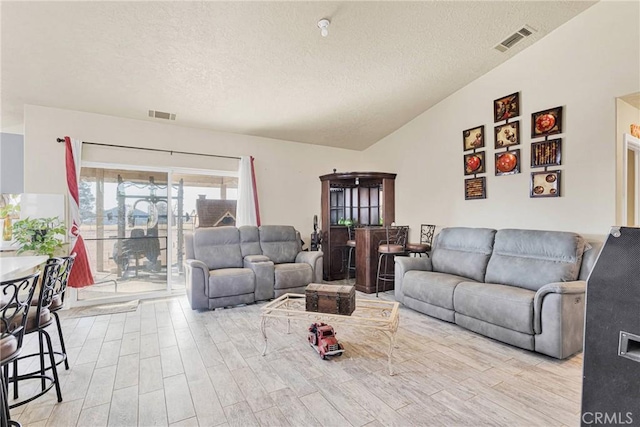 living room with vaulted ceiling, light hardwood / wood-style floors, and a textured ceiling