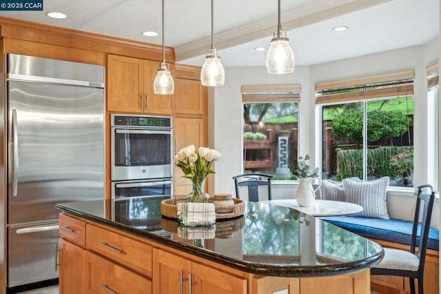 kitchen with stainless steel appliances, a kitchen island, hanging light fixtures, and dark stone counters