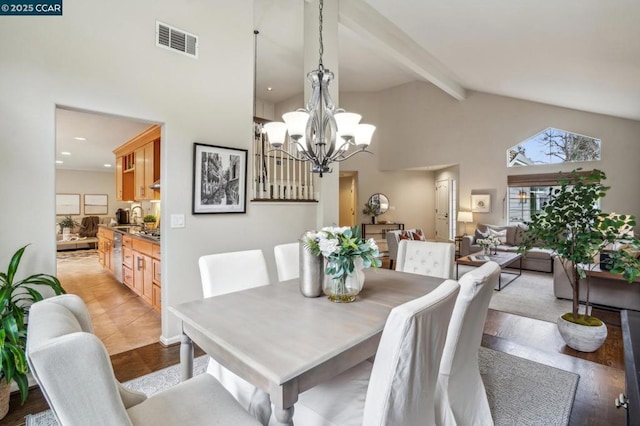 dining space with an inviting chandelier, high vaulted ceiling, beamed ceiling, and light wood-type flooring